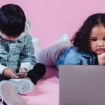 A young boy with a phone and a young girl with a laptop